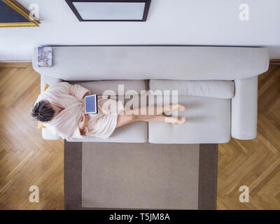 Mature woman in bathrobe sitting on the couch at home using digital tablet Stock Photo