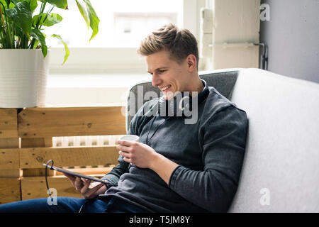 Smiling young man with tablet and headphones sitting on couch Stock Photo