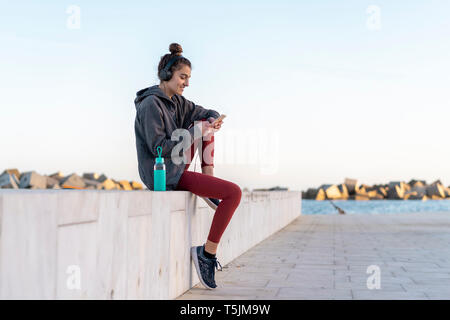 Sportive young woman with headphones during workout, using smartphone Stock Photo
