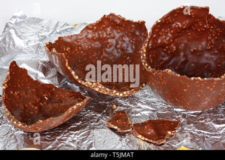 Broken chocolate Easter egg with chopped hazelnuts on a foil sheet against, UK. Stock Photo