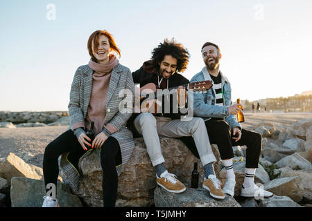 Three happy friends with guitar sitting outdoors at sunset Stock Photo