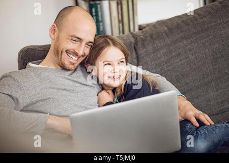 Father and daughter sitting on couch, using laptop Stock Photo