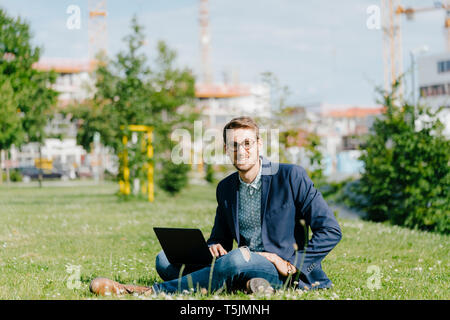 Young businessman sitting in park, using laptop Stock Photo
