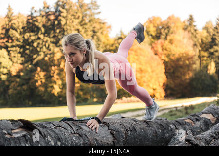 Young woman doing pushups on tree trunk during workout in nature Stock Photo