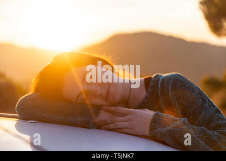 Young woman on a road trip, taking a break, resting on car Stock Photo