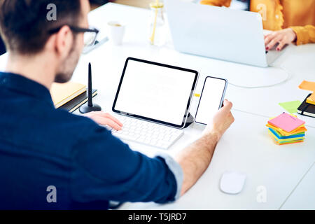Businessman working on smartphone and tablet at desk in office Stock Photo