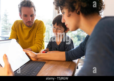 Family sitting at table, using digital tablet Stock Photo