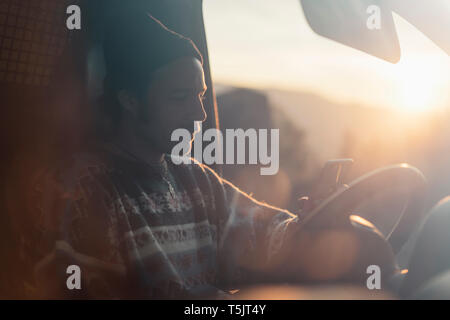 Young man on a road trip, using smartphone Stock Photo