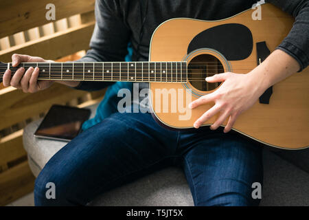 Close-up of man sitting on couch playing guitar Stock Photo