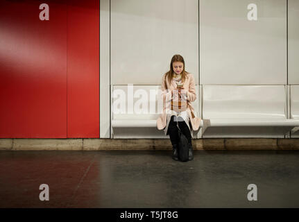 Austria, Vienna, young woman waiting at underground station using smartphone Stock Photo