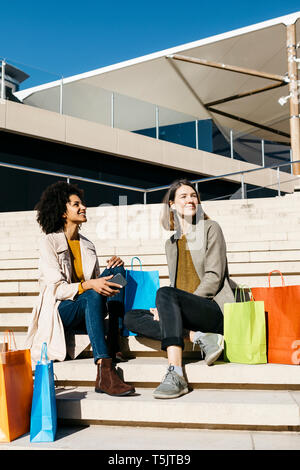 Two happy women with shopping bags sitting on stairs Stock Photo