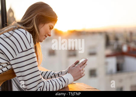 Young woman on balcony at sunset using mobile phone Stock Photo