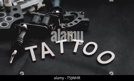 Tattoo accessories With the inscription tattoo of wooden letters on a black background. Stock Photo