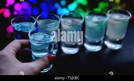 Female hand with a shot of alcohol, neon blurred background in bar Stock Photo