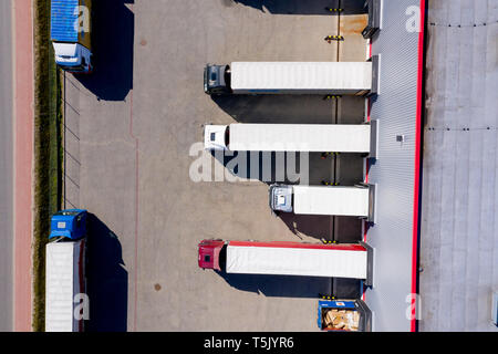 Aerial Side Shot of Industrial Warehouse Loading Dock where Many Truck with Semi Trailers Load/ Unload Merchandise Stock Photo