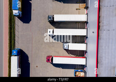 Aerial Side Shot of Industrial Warehouse Loading Dock where Many Truck with Semi Trailers Load/ Unload Merchandise Stock Photo