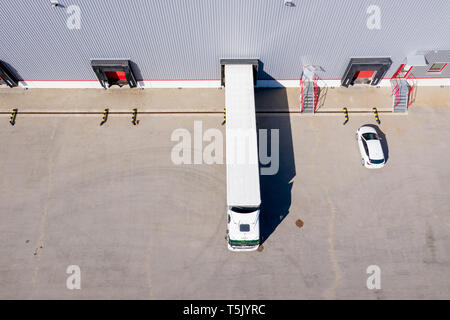 Aerial Side Shot of Industrial Warehouse Loading Dock where Many Truck with Semi Trailers Load/ Unload Merchandise Stock Photo