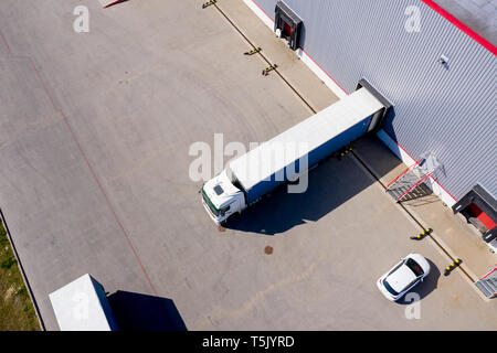 Aerial Side Shot of Industrial Warehouse Loading Dock where Many Truck with Semi Trailers Load/ Unload Merchandise Stock Photo