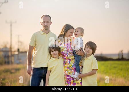Beautiful family, mother, father and three kids, boys, having familly outdoors portrait taken on a sunny spring evening, beautiful blooming garden, su Stock Photo