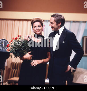 Der Schauspieler, Entertainer und Synchronsprecher Harald Juhnke posiert mit seiner Frau Chariklia Baxevanos in einem Wohnzimmer oder an einem Set, Deutschland 1970er. The actor, entertainer and voice actor Harald Juhnke poses with his wife Chariklia Baxevanos in a living room or on a set, Germany 1970s. Stock Photo