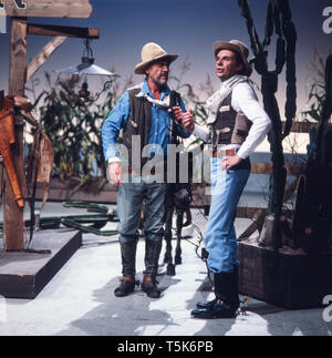 Der Schauspieler, Entertainer und Synchronsprecher Harald Juhnke als Cowboy verkleidet bei einem Auftritt oder Sketch mit Ken Curtis (Festus Haggen) aus der Fernsehserie Rauchende Colts, Deutschland 1970er. The actor, entertainer and voice actor Harald Juhnke dressed as a cowboy during a performance or sketch with Ken Curtis (Festus Haggen) from the TV series Gunsmoke, Germany 1970s. Stock Photo