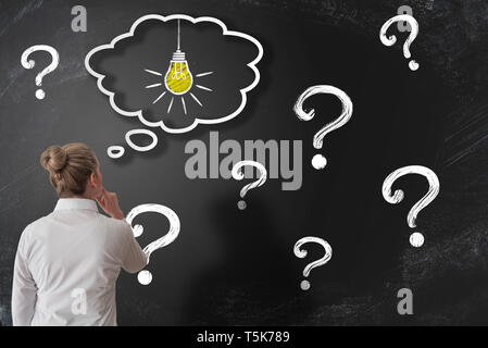 finding solution to problem or answer to question concept with woman looking at chalkboard with question marks while having an idea Stock Photo