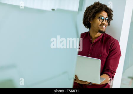 Happy young handsome African American IT specialist wearing glasses working on his laptop in the office Stock Photo