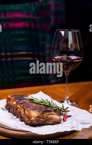 Striploin grilled beef steak served with rosemary, salt and peppercorns on wooden board with glass of wine. Stock Photo