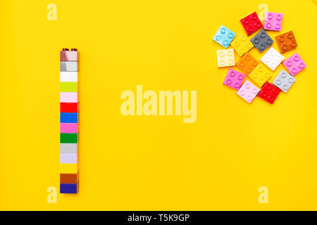 Colorful plastic construction of square block elements of toy constructor with separate bricks on yellow background with copy space. Flat lay style. T Stock Photo