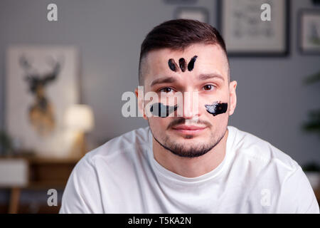 The black coal mask film on the face of a Caucasian male brunette looks like an Indian ornament. Concept male skin care, metrosexual, beauty salon Stock Photo