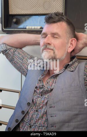 portrait of handsome man in his 50s relaxing next to vintage radio Stock Photo