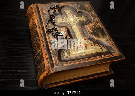 Ancient leather bound Holy Bible with Rosary beads on black oak table Stock Photo