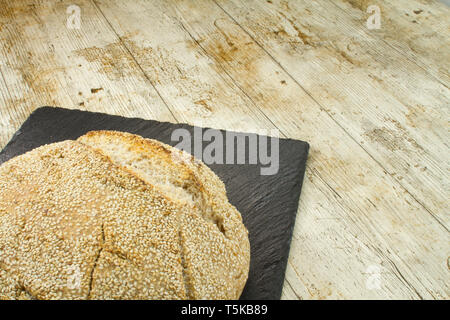 Close-up of a loaf of homemade bread with sesame seeds in selective focus on wooden table background Stock Photo