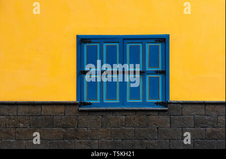 A colourful closed blue window with yellow wall and black stone bricks underneath in the historic city center of Cuenca, Ecuador. Stock Photo