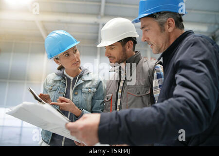 Team of construction workers talking in empty warehouse Stock Photo