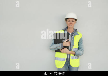Smiling female construction worker in safety gear on grey background Stock Photo