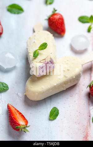 Strawberry ice cream on stick covered with white chocolate on marble table, flat lay Stock Photo