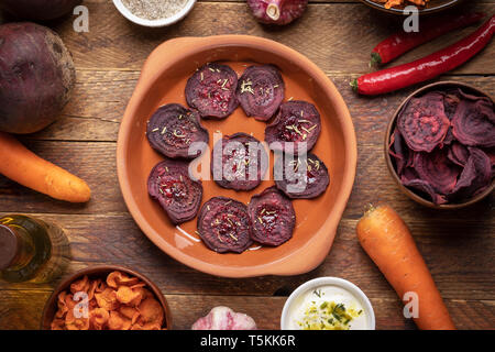 Plate and cups with healthy homemade  vegetable chips and  whole vegetables on wooden background.   Stock Photo