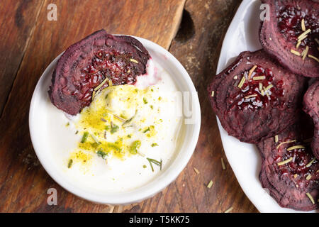Close-up beetroot chips in cup with sour cream sauces and on white plate on wooden background.   Stock Photo