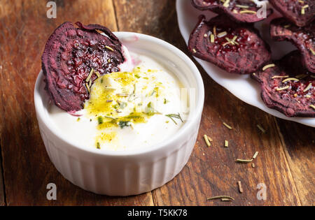 Close-up beetroot chips in white cup with sour cream sauce and on white plate on wooden background.   Stock Photo