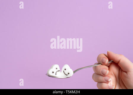 spoon with a piece of sugar in a female hand on a lilac background Stock Photo