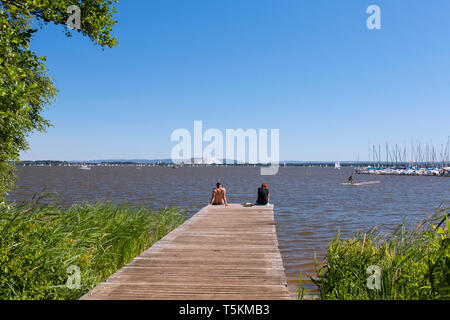 Couple sitting on jetty at Lake Steinhude / Steinhuder Meer in summer, Mardorf, Lower Saxony / Niedersachsen, Germany Stock Photo