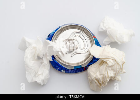 Crushed compressed aluminum can of a carbonated drink with crumpled sheets of paper. Pollution, waste, ecology. Stock Photo