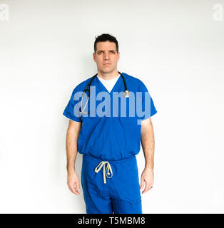 Medical doctor in surgical scrubs standing against a white backdrop. Stock Photo