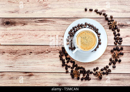 Top view of a cup of hot coffee on wooden rustic table with spilled coffee beans and anise. Space for text . Stock Photo
