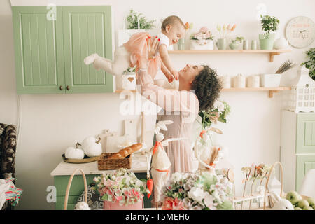 Happy mother plays with her baby in the kitchen on background of easter decorations. Stock Photo
