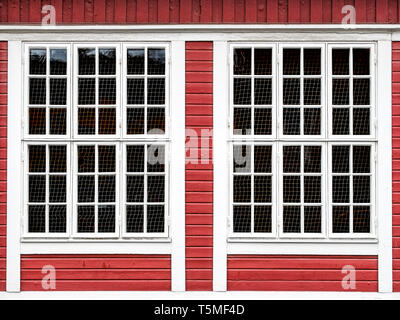Big windows on a red wooden wall, with white framing along the windows. Stock Photo