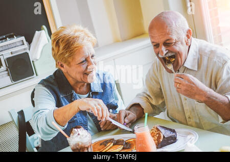 Happy seniors couple eating pancakes in a bar restaurant - Mature people having fun dining together at home - Concept of elderly lifestyle moments Stock Photo