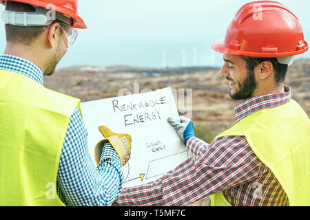 Workers engineers reading and talking about the new renewable energy project - Two builders discussing how to build windmill and panels solar Stock Photo