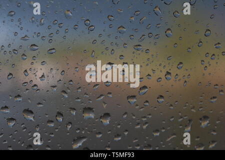 Focus on the rain on a window with blurred coloured background of the reflections beyond forming a bokeh effect Stock Photo